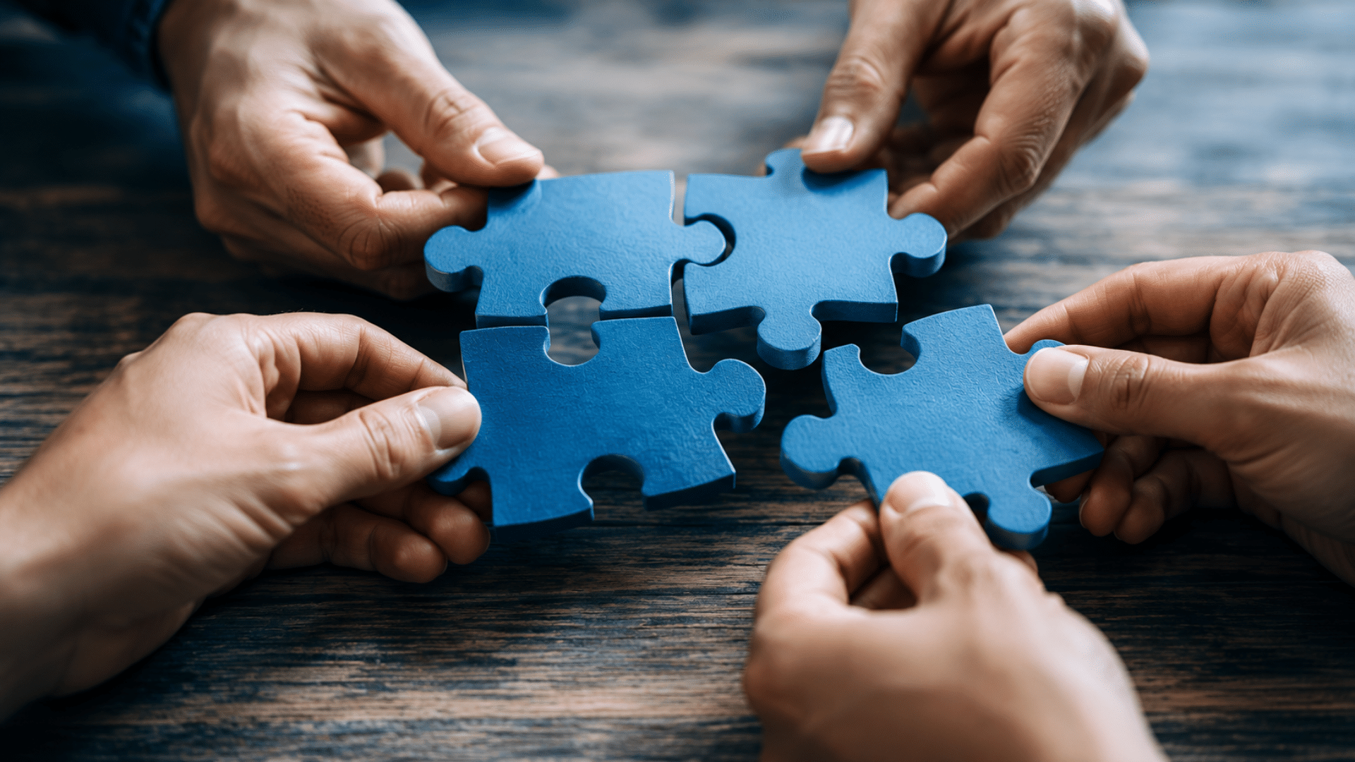 People collaborate to fit blue puzzle pieces together, symbolizing teamwork and problem solving.